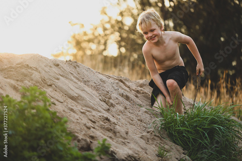 Cheeky caucasion boy playing in sand dunes with shirt off. Wildling childhood. 