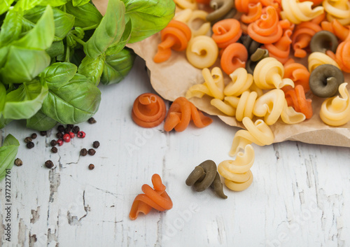 Fototapeta Naklejka Na Ścianę i Meble -  Raw homemade tricolore trottole pasta in brown paper on white wooden background with basil.