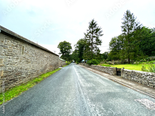 View along, Hawthorns Lane, with old stone buildings, gardens and trees in, Malham, Skipton, UK