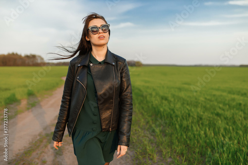 Full length portrait of a stylish girl walking along a green field. A young smiling woman is walking in nature. Green spring meadow