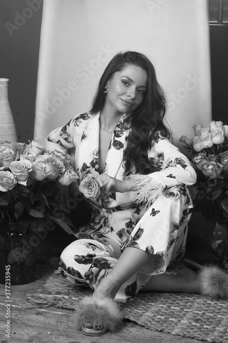 Young woman in floral design pyjamas costume sitting at wooden floor at home with lots of roses. Fashion style portrait with smoke or fog and colorful lightning