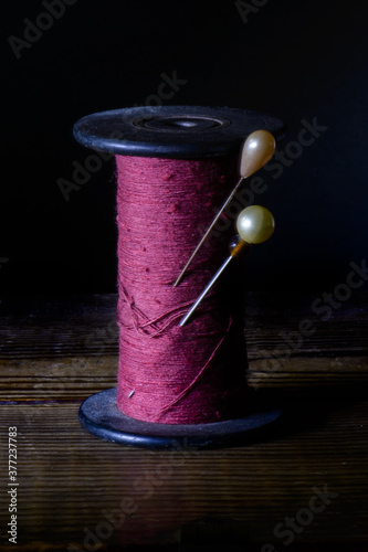 Vintage spool of thread, magenta color, with two old pearl hat pins in it. photo