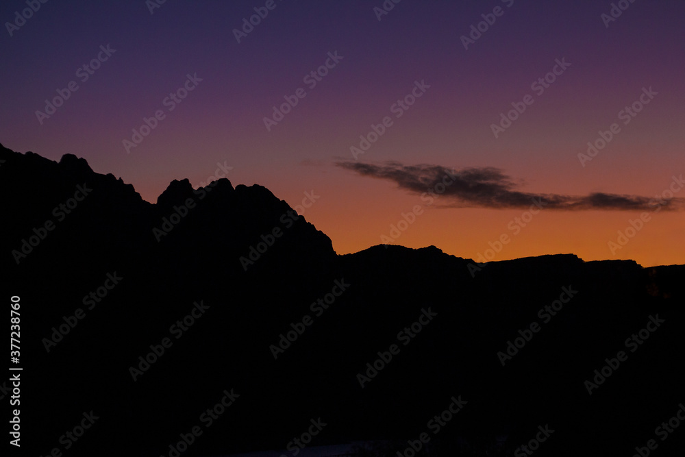 Beautiful sunset in the mountains. Violet and orange colors of the blue hour with a cloud and the silhouette of the Andes Mountains in Mendoza, Argentina.