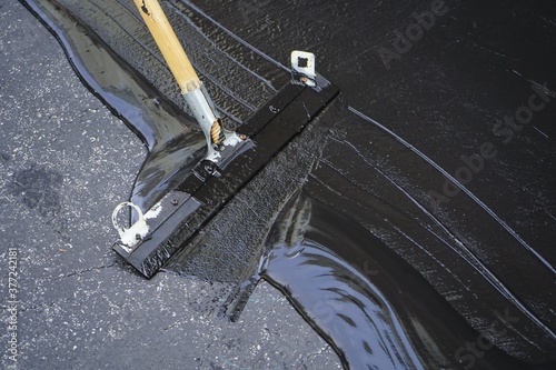 Man sealing asphalt driveway/Sealcoating