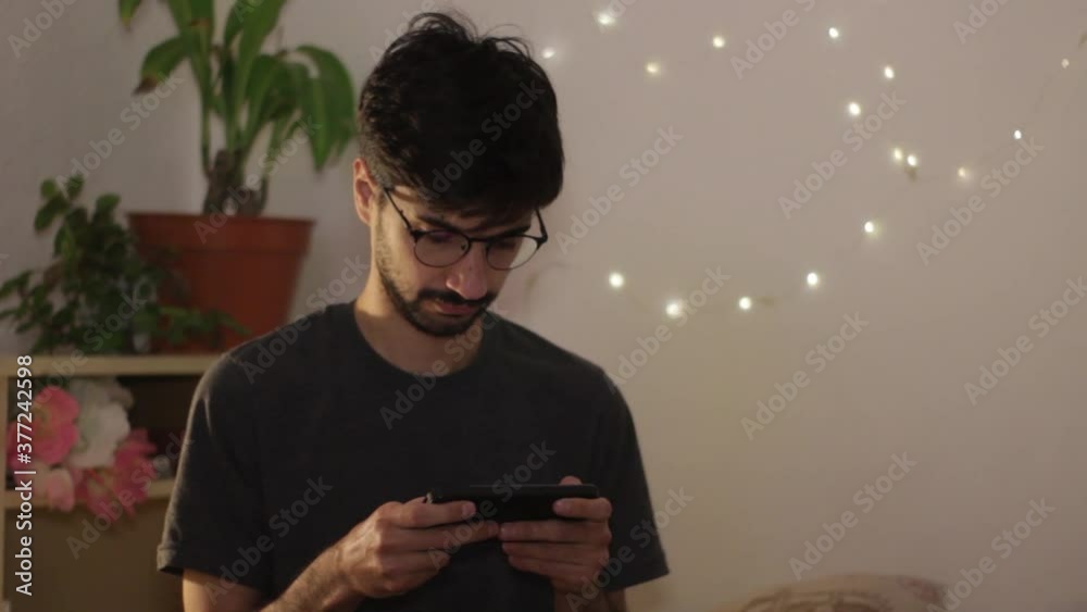 Young millenial handsome man plays a videogame in smartphone or texts message 