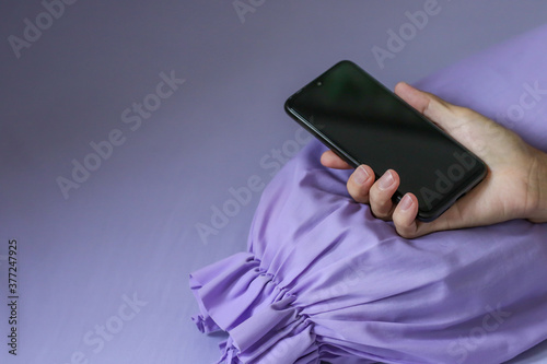A black smartphone in man hand on purple bed photo