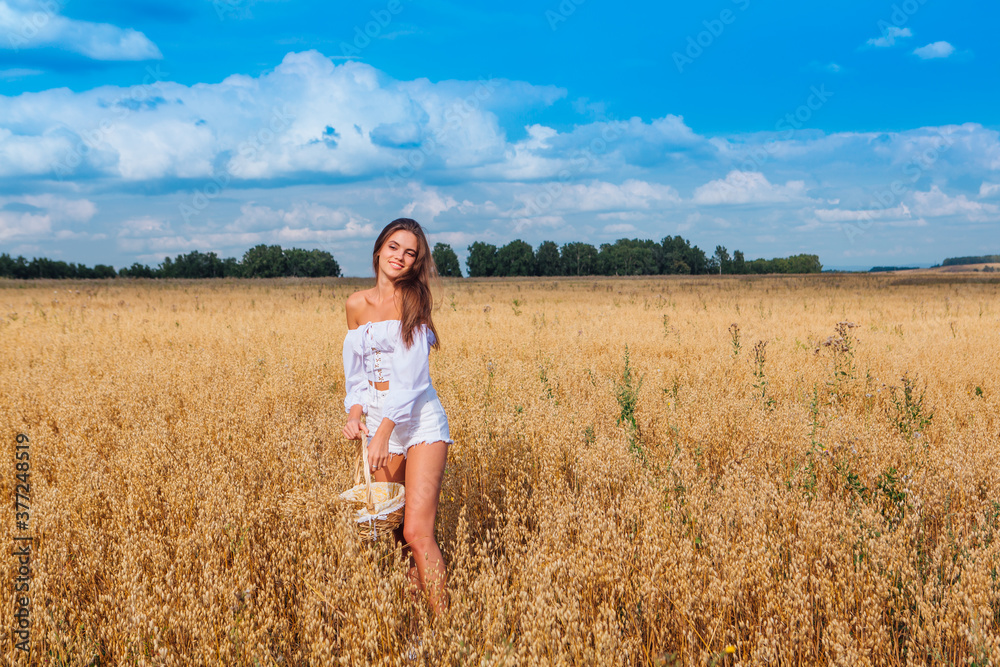 Young beautiful woman at golden oat field holding basket with ears of oats.