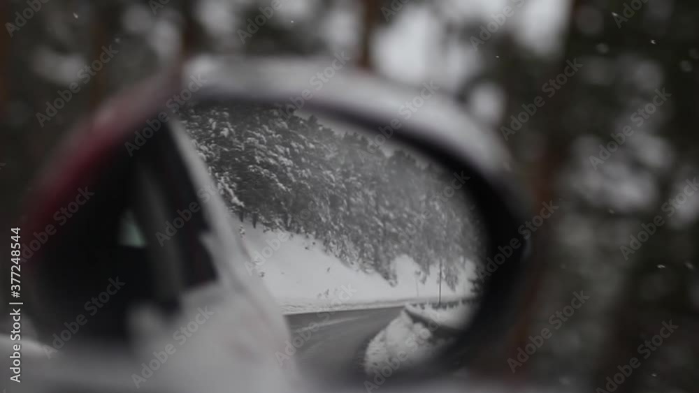 Close up side mirror, snowy road, trees at the background, road trip in the mountains Close up side mirror, snowy road, trees at the background, road trip in the mountains