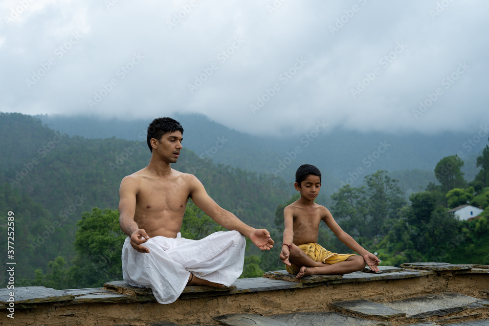 A young man sitting on the roof with his younger brother,both wearing dhoti, smiling into the camera