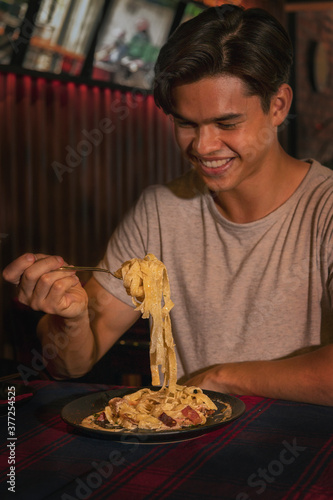 An action shoot of a young handsome man is enjoying his food carbonara pasta in a restaurant