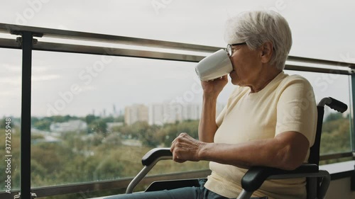 Wallpaper Mural Senior gray haired woman with eyeglasses drinking cup of coffee in the wheelchair in front of the window. High quality 4k footage Torontodigital.ca