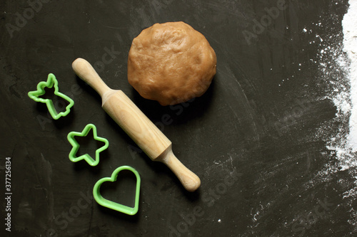 Dough, rolling pin and cookie molds on a black background. Ginger cookie dough on a floured black surface. View from above. The dough has a brown tint. The concept of cooking. Copying space for text