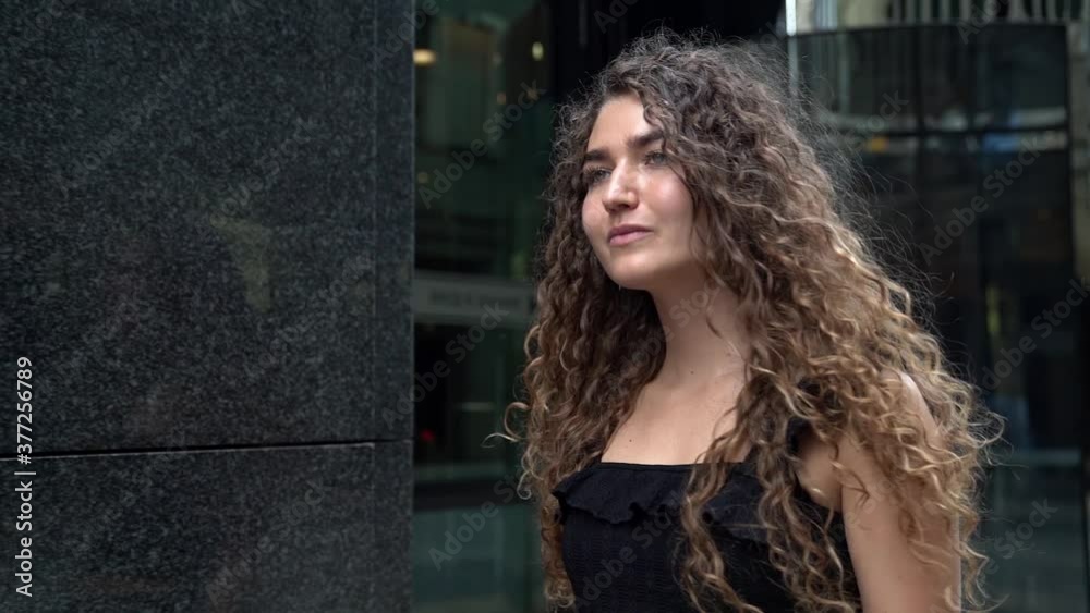 A beautiful young woman with curly hair walks along a city street in the background of a building. Straightens her hair. A beautiful young woman with curly hair walks along a city street in the background of a building. Straightens her hair.