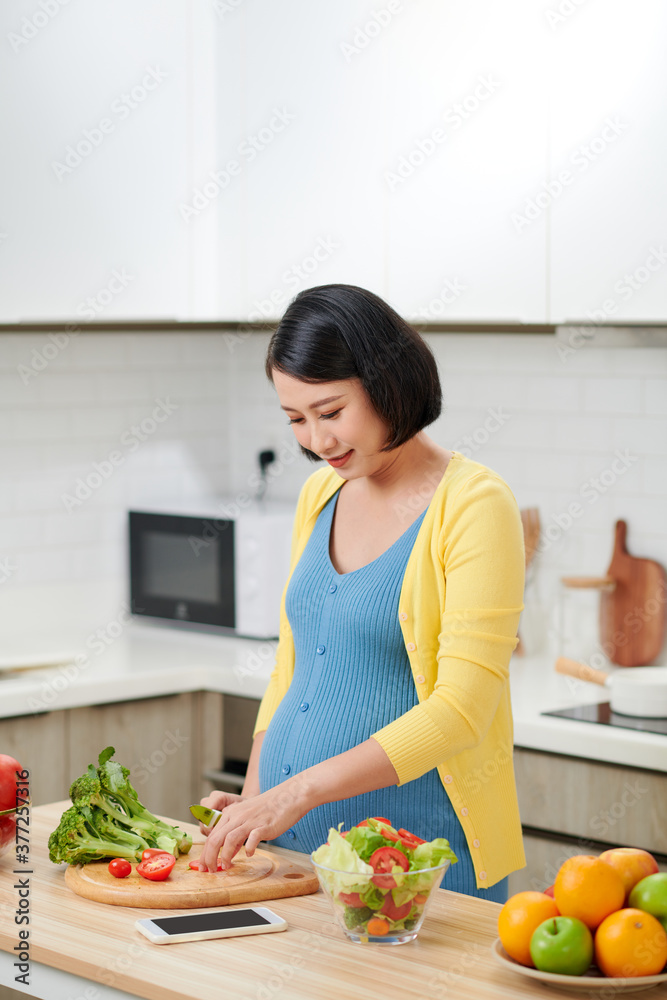 Pregnant Woman Mixing Fresh Green Salad On Kitchen.