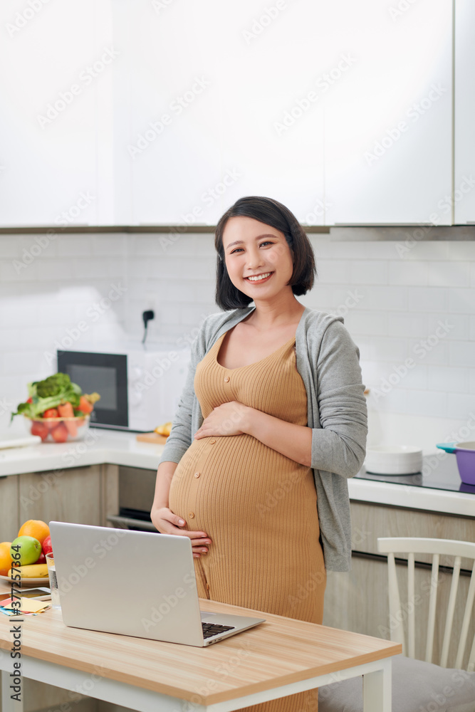 Beautiful pregnant woman with laptop in kitchen