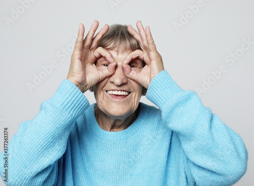 An elderly woman makes glasses from her fingers, amuses herself and poses. A fun time at any age.