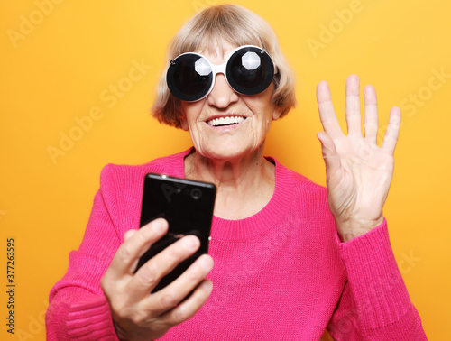 old grandmother is talking to her grandchildren by phone, smiling and greeting them.