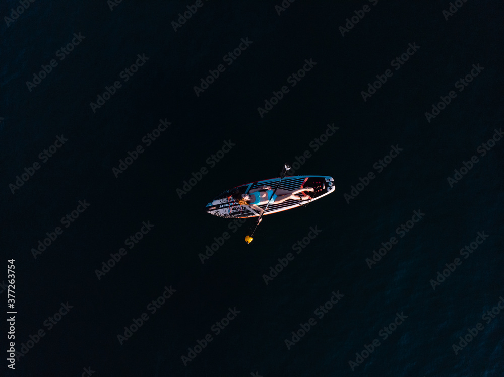Naklejka premium Attractive Woman on Stand Up Paddle Board, Woman paddling on sup board and enjoying turquoise transparent water. Tropical travel, wanderlust and water activity concept. Sunset and relax
