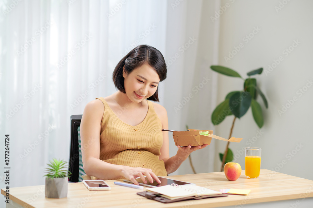 Young pregnant woman using digital tablet eating fresh salad and fruits on table Young pregnant woman using digital tablet eating fresh salad and fruits on table