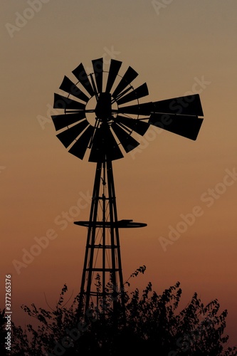 windmill at sunset with tree's north of Hutchinson Kansas USA out in the country.