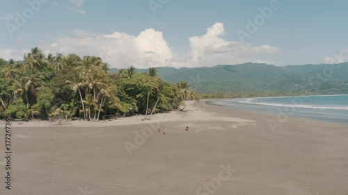 Drone aerial flying low and perople playing at a the beautiful beach with palm trees in costa rica photo