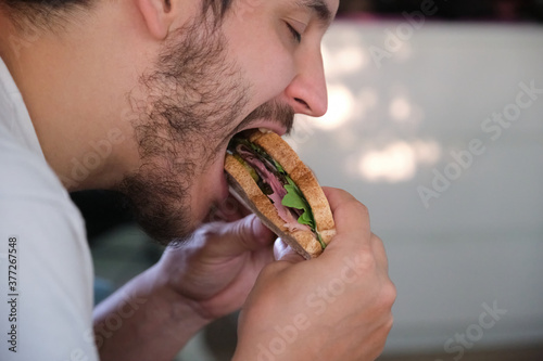 Close up of a young man eating a pastrami sandwich. Fast food concept.