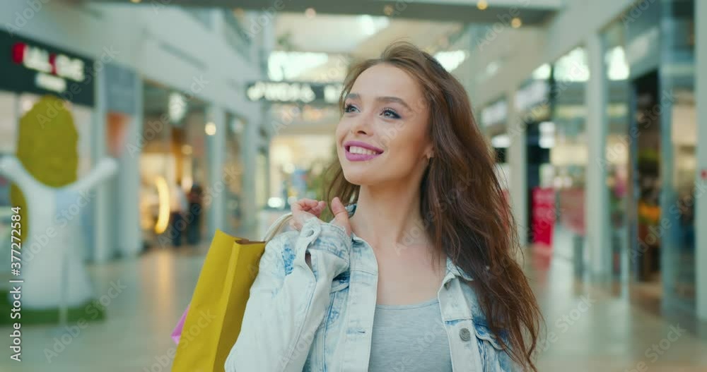 The girl is smiling and walking through the shopping center. She is throwing shopping bags over her shoulder. 4K The girl is smiling and walking through the shopping center. She is throwing shopping bags over her shoulder. 4K