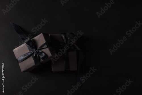 Black Friday sale shopping concept, Top view of gift box wrapped in black paper and black bow ribbon, studio shot on black background
