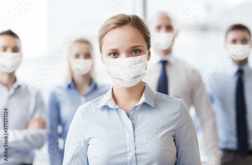 business, people and pandemic concept - businesswoman wearing face protective medical mask for protection from virus disease with group of businesspeople in office