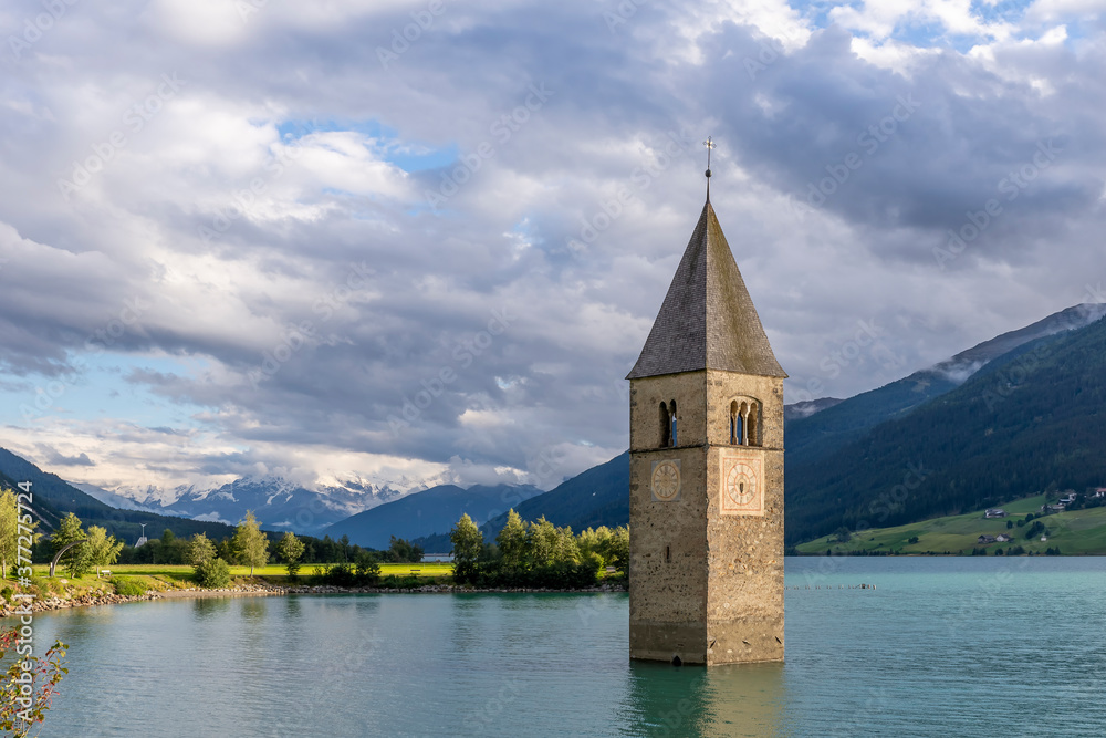 The famous bell tower of old Curon, submerged in Lake Resia, South Tyrol, Italy, with the snow capped Alps in the background