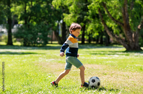 childhood, leisure games and people concept - happy little boy with ball playing soccer at summer park