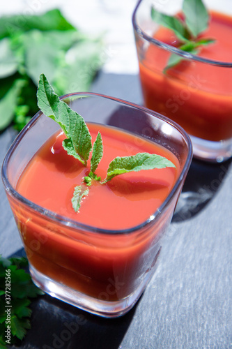 2 glasses of fresh tomato juice with mint and parsley on a black, top view. Vegan, healthy lifestyle concept