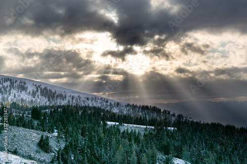High contrasted snowy mountain landscape. The sun's rays break through the clouds. Alpe del Nevegal, Belluno, Italy