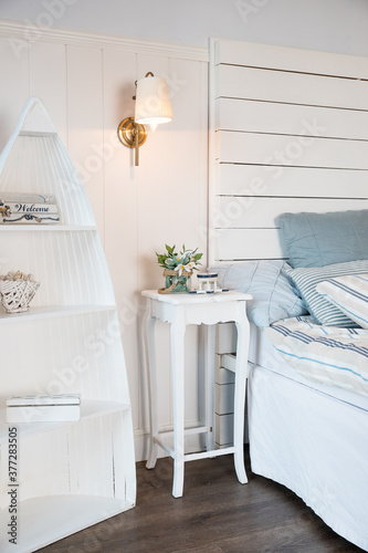 Bright and comfortable bedroom interior design in scandinavian style.Flowers on bedside table. Pillow on bed decoration room interior. Burning small lamp above a table.