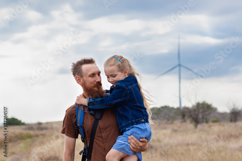 Father with daughter in hands standing on a hill with nature lanscape. Little blonde girl smiling and hugging with dad outdoor. Loving child embrace her daddy. Father's Day family greeting card.