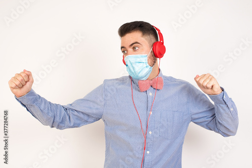 Young man wearing casual clothes against orange wall, dancing and listening music with headphones. photo