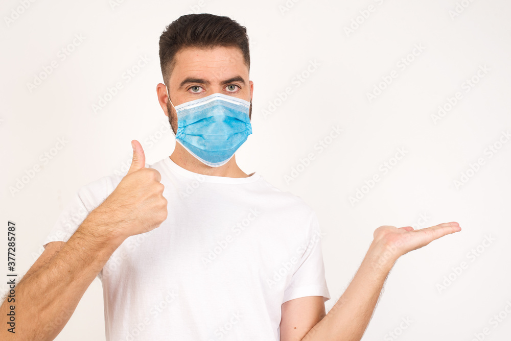 Young happy cheerful man showing thumb up and pointing with the other hand while standing indoors. Good Job. Wearing casual clothes. Young happy cheerful man showing thumb up and pointing with the other hand while standing indoors. Good Job. Wearing casual clothes.