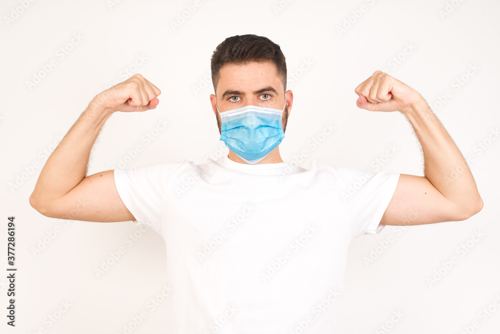 Waist up shot of caucasian man raises arms to show his muscles feels confident in victory, looks strong and independent, smiles positively at camera, stands against gray background. Sport concept.