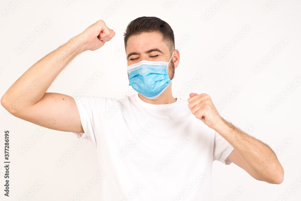 Attractive young caucasian man celebrating a victory punching the air with his fists and a beaming toothy smile over a gray studio background with copy space Attractive young caucasian man celebrating a victory punching the air with his fists and a beaming toothy smile over a gray studio background with copy space