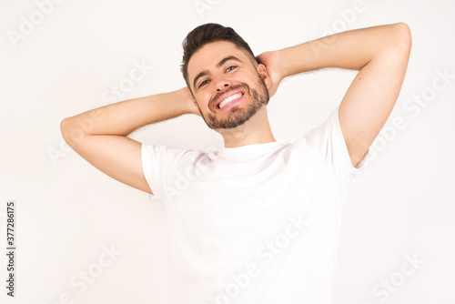 Confidence and coquettish concept. Portrait of charming young man, smiling broadly with self-assured expression while holding hands over her head. Standing against gray background.