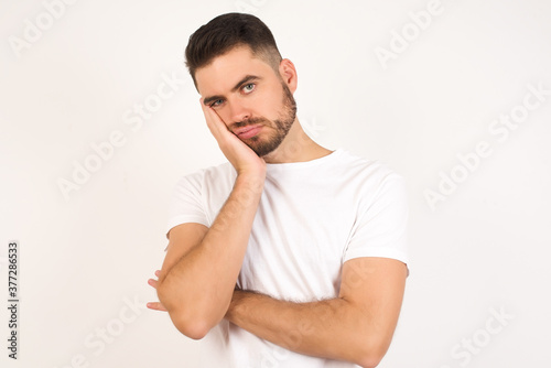 Very bored adult man with beard holding hand on cheek while support it with another crossed hand, looking tired and sick, over gray background. Father attends parents day at school