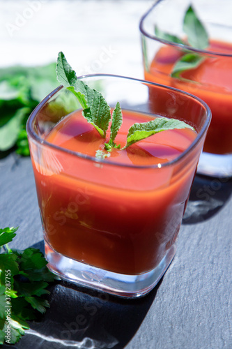 2 glasses of fresh tomato juice with mint and parsley on a black, top view. Vegan, healthy lifestyle concept