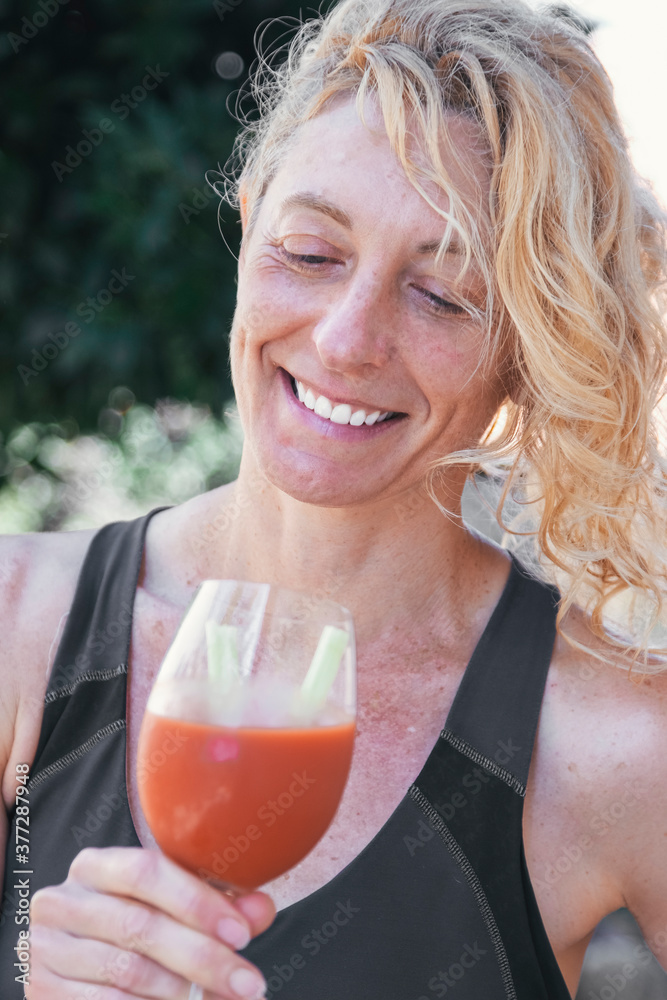 Young mature blonde woman in sportswear outdoor with a glass of tomato juice. Young mature blonde woman in sportswear outdoor with a glass of tomato juice.