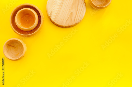 Set of rustic wooden tableware - bowls and utensils on yellow background top view