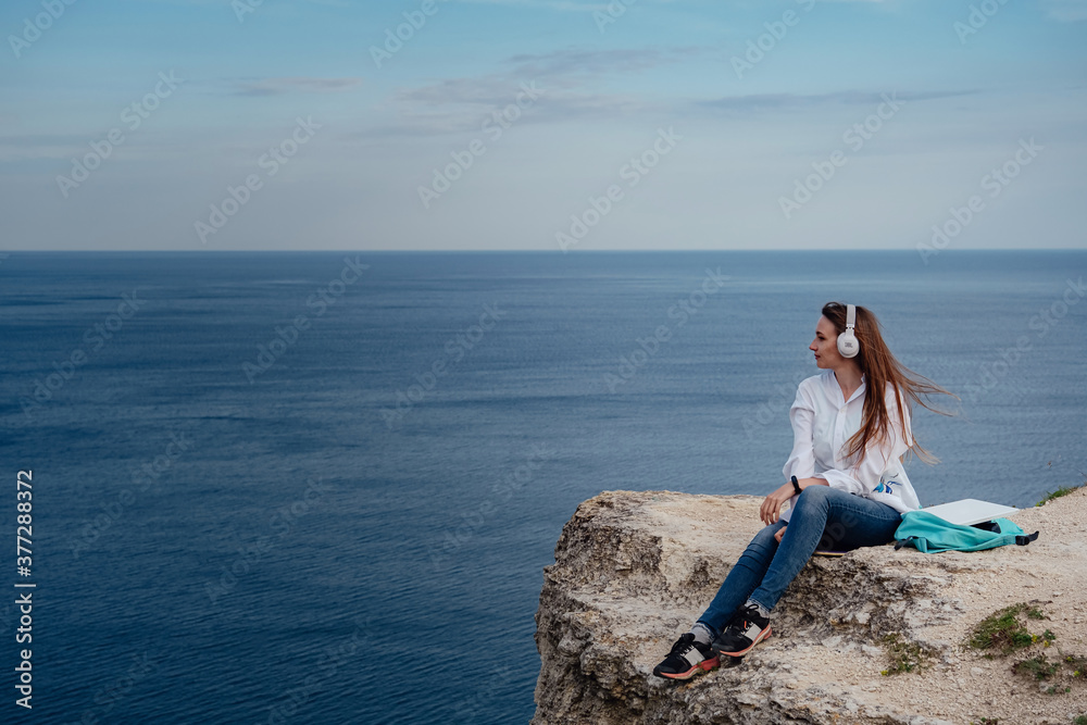 Young business woman working at the computer on the beach on the rock face.