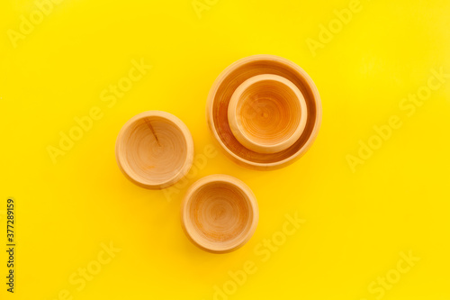 Set of rustic wooden tableware - bowls and utensils on yellow background top view