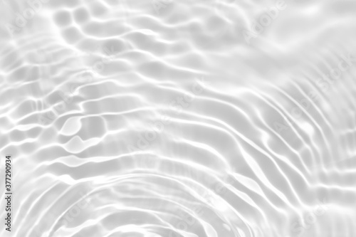 Blurred desaturated transparent clear calm water surface texture with splashes and bubbles. Trendy abstract nature background. White-grey water waves in sunlight. Copy space.