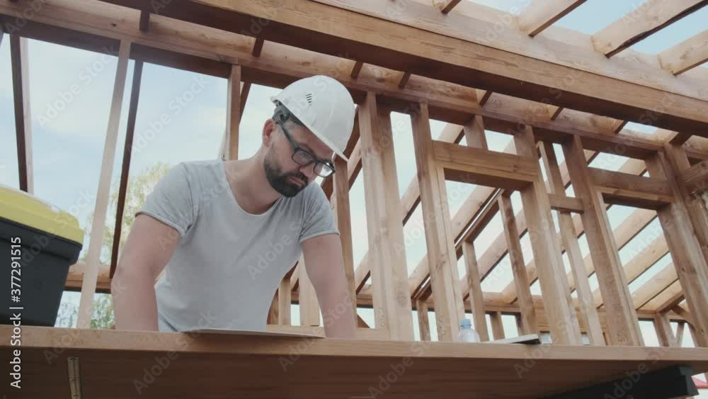 Man builds a wooden house, makes a project in a helmet. Mid-shot