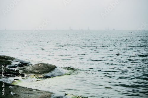 sailboats and sea and rocks on a foggy day