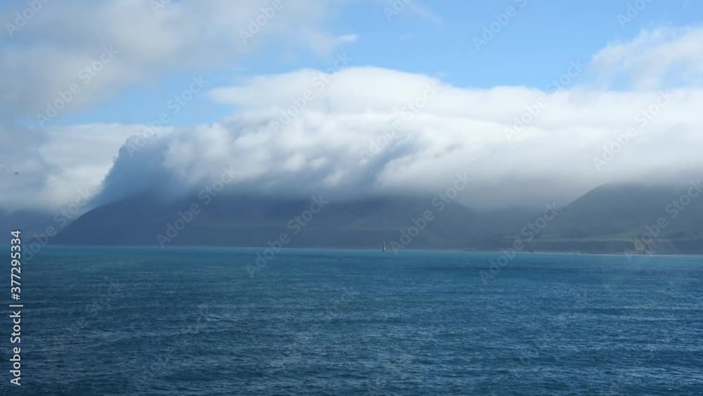 Long white clouds hanging over the cliffs at the shore of the North Island of New Zealand. Viewn from the sea Long white clouds hanging over the cliffs at the shore of the North Island of New Zealand. Viewn from the sea